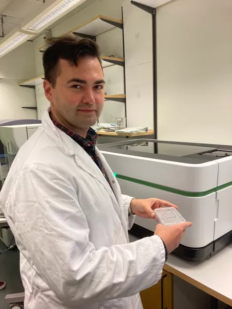 Photo of Roman Sattarov with his cell culture plate in front of the Operetta machine. 